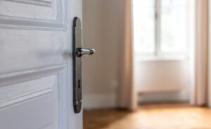 Door knob on white retro door, close up. Door open, blur room interior, window and wood floor